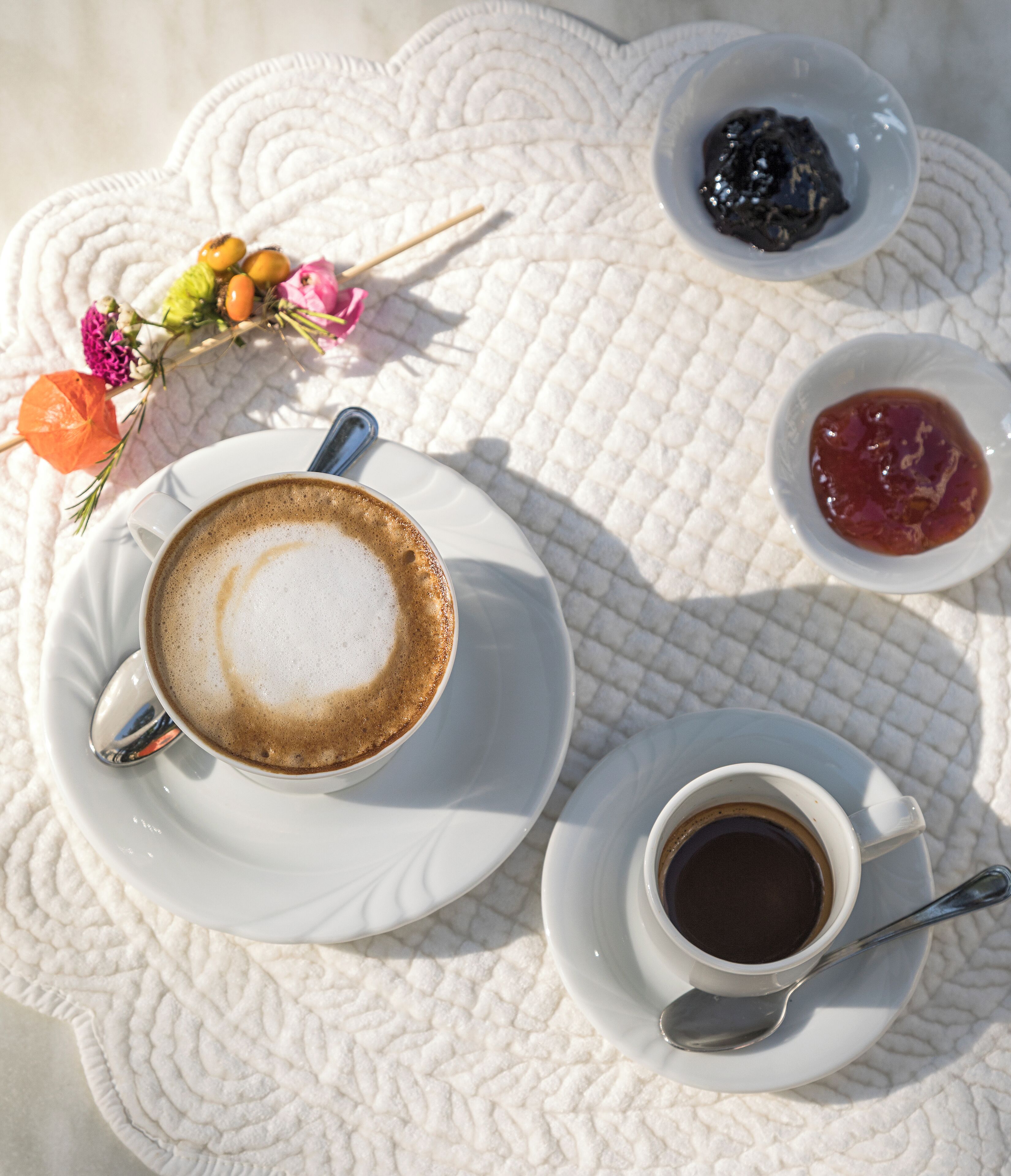 A table with two cups of coffee, one with milk and one without, and two small bowls of jam.