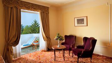 A room with a balcony, a table with fruit, two chairs, and a framed picture on the wall.