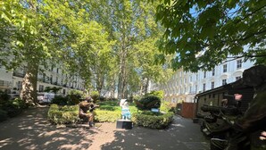 A park with a statue of a man taking a photograph, surrounded by trees and a pathway. - Tudor Court Hotel (London)