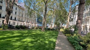 A paved pathway flanked by lush green grass and trees, leading to a row of white buildings with balconies. - Tudor Court Hotel (London)