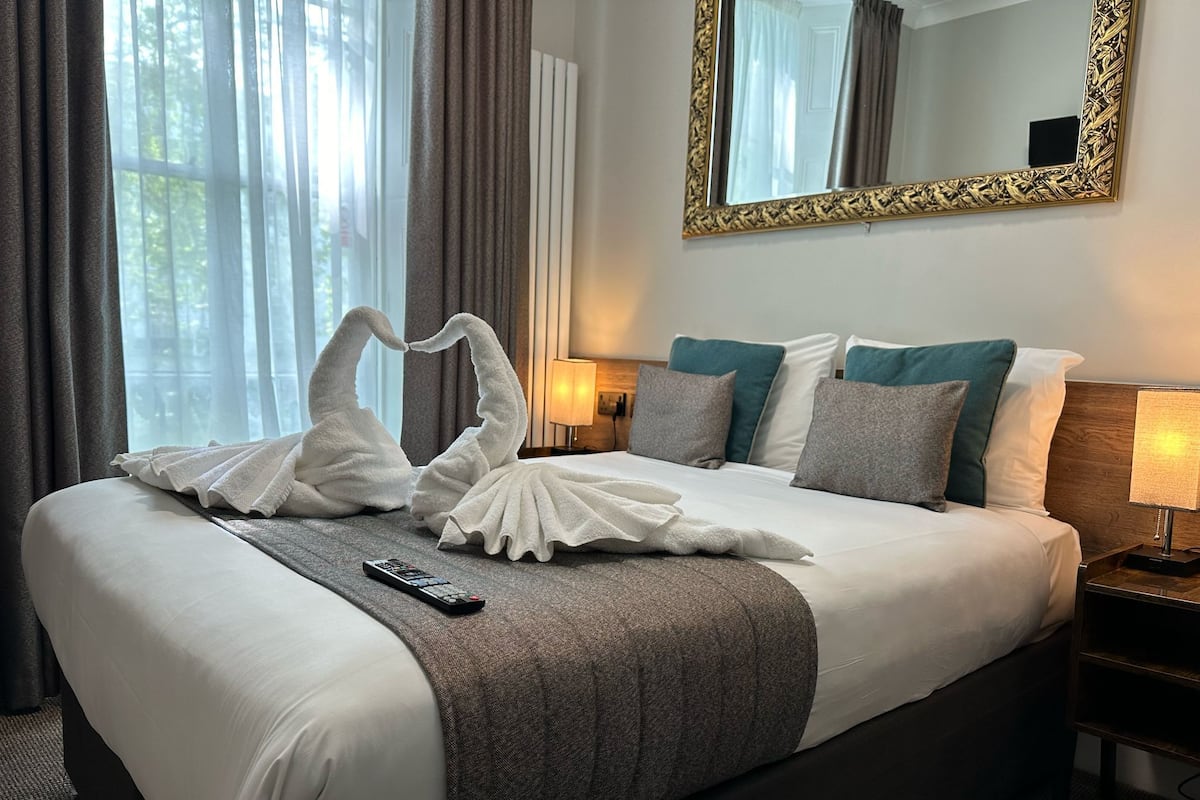 A hotel room with a large bed, a remote control, and a mirror on the wall.