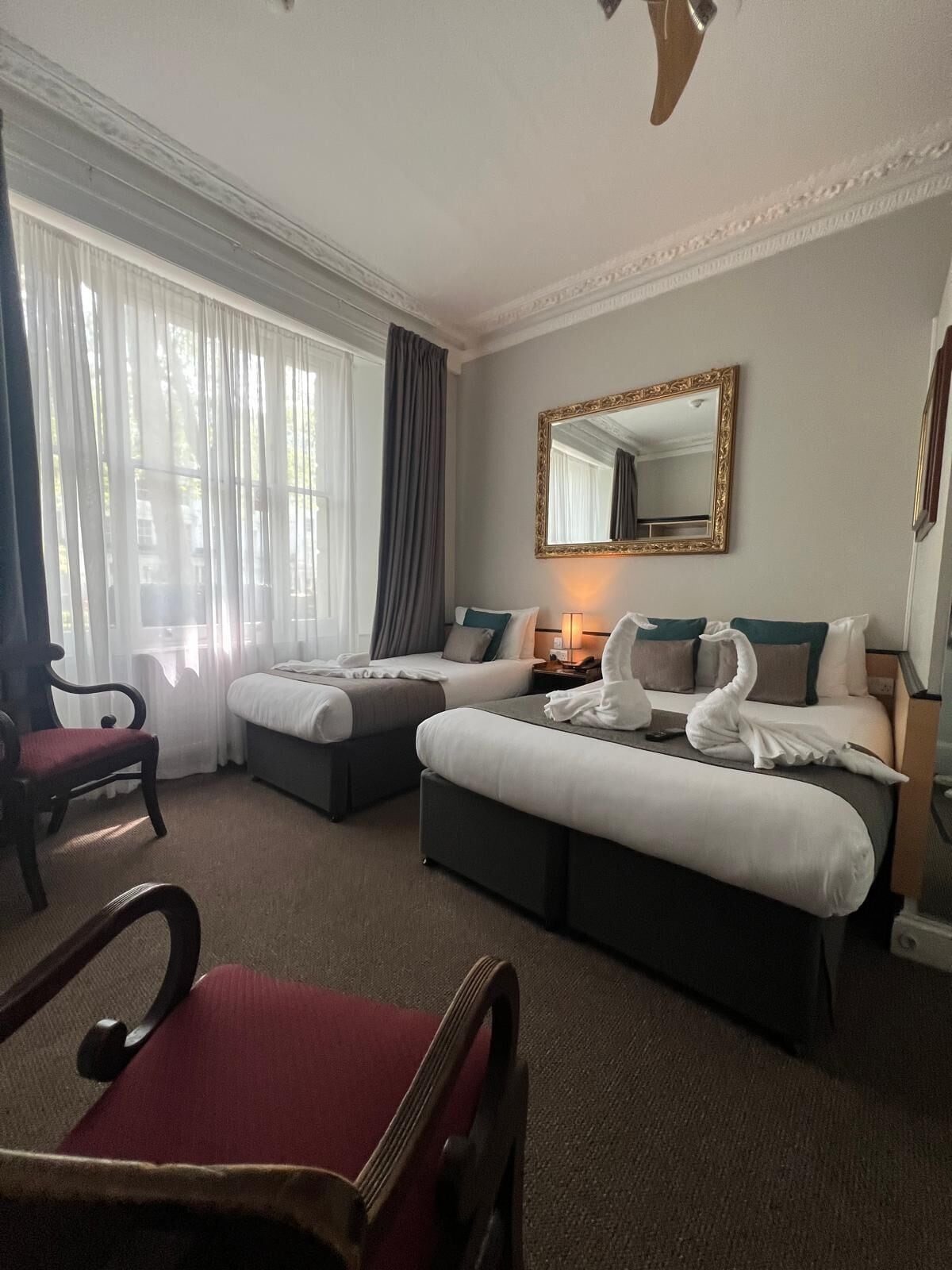 A hotel room with two beds, a desk, a chair, and a large window with curtains.