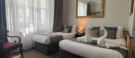 A hotel room with two beds, a desk, a chair, and a large window with curtains.