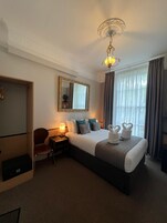 Quarto de hotel com uma cama grande, uma escrivaninha, uma cadeira, um guarda-roupa e um espelho.