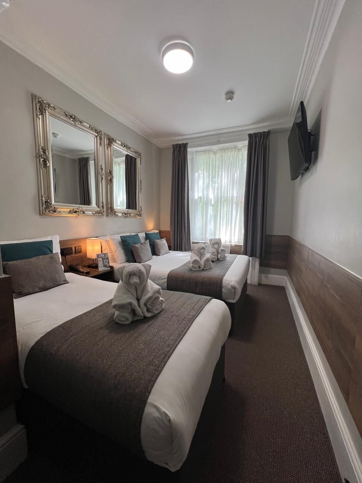 A hotel room with two beds, a large mirror, a flat-screen TV, and a window with curtains.