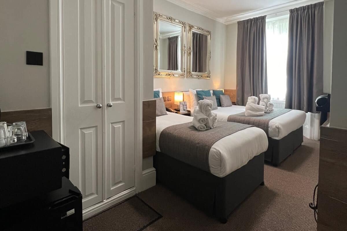 A hotel room with two beds, a wardrobe, a desk with a lamp, and a large mirror.