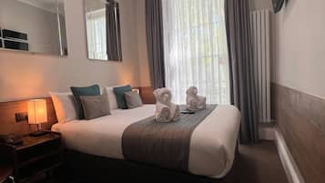 Une chambre d’hôtel avec un grand lit, une table de chevet avec une lampe, un téléviseur à écran plat fixé au mur et une fenêtre avec des rideaux.