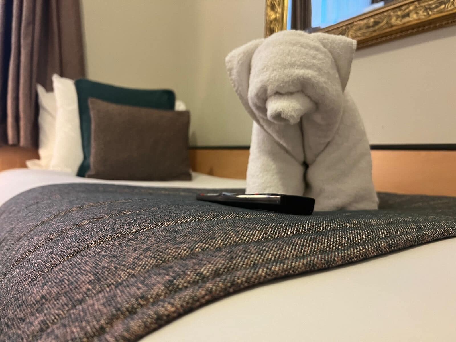 A hotel room with a bed, a remote control, and a plush toy on the bed.