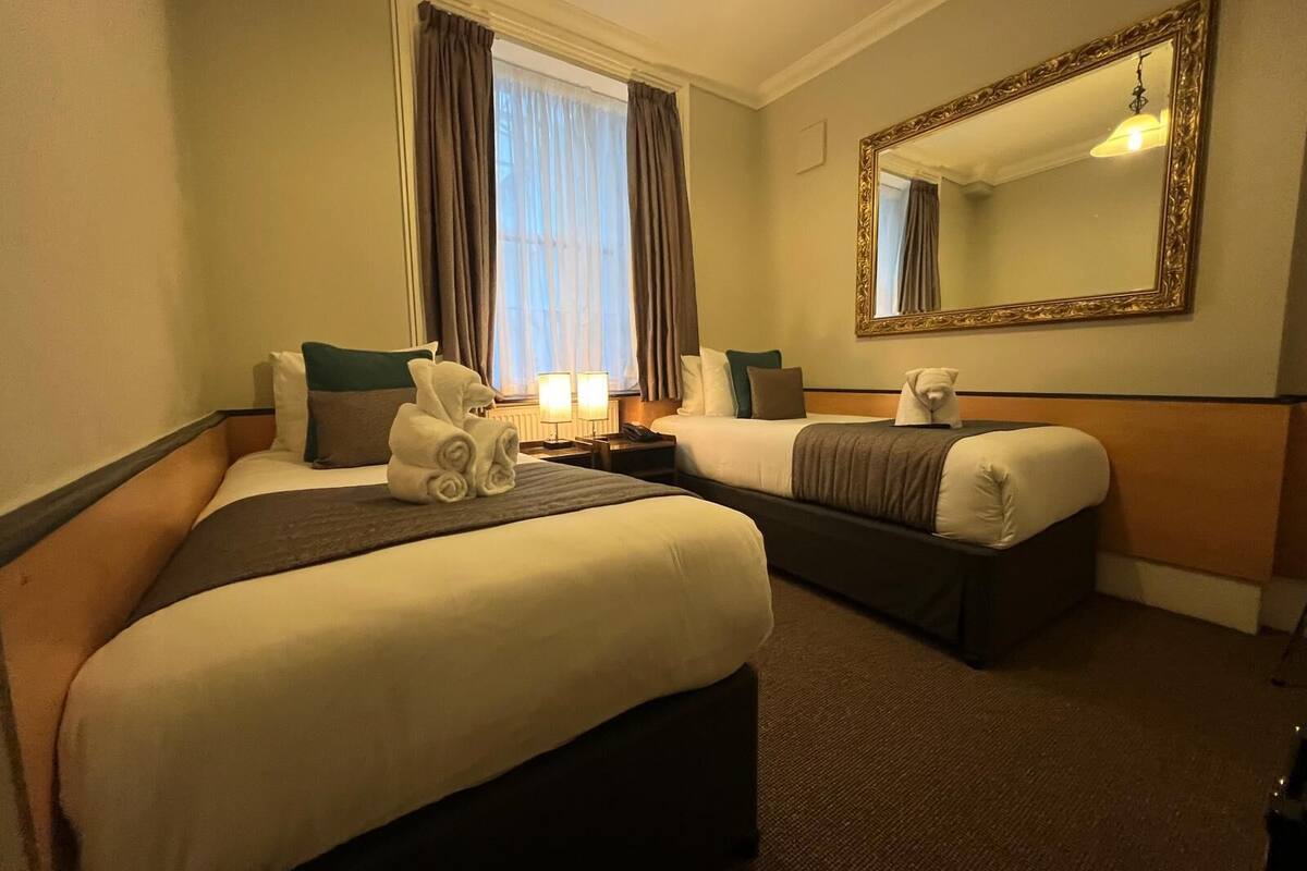A hotel room with two beds, a large mirror, and a window with curtains.