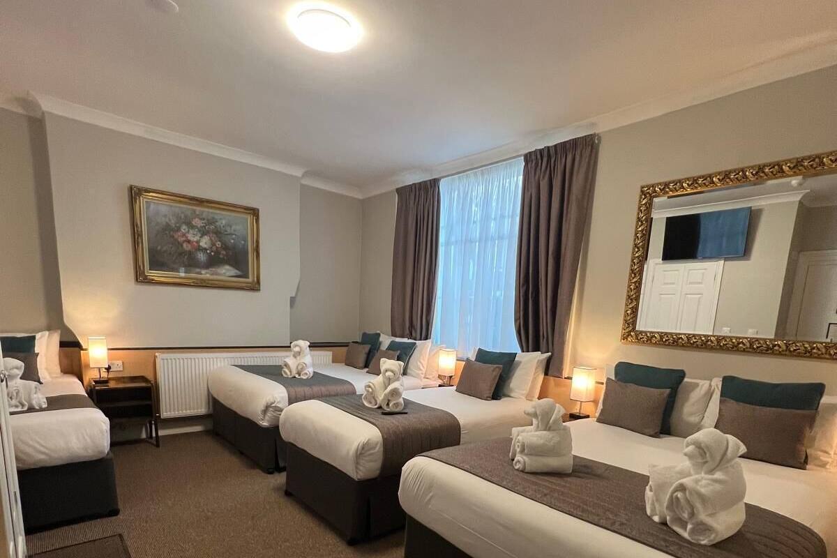 A hotel room with three beds, a desk, a chair, a large mirror, and a painting on the wall.