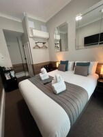 A hotel room with a large bed, a bedside table, a mirror, and a wall-mounted TV.