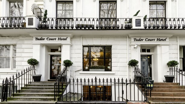 A two-story Tudor Court Hotel with a symmetrical facade, black wrought iron balconies, and a classic architectural style. - Tudor Court Hotel (London)