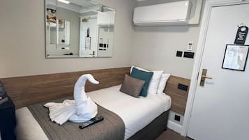 A hotel room with a bed, a mirror, an air conditioning unit, a door with a sign, and a remote control on the bed.