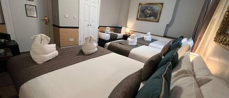 A hotel room with two beds, a flat-screen TV mounted above the left bed, a painting on the wall, and a door with a nameplate.