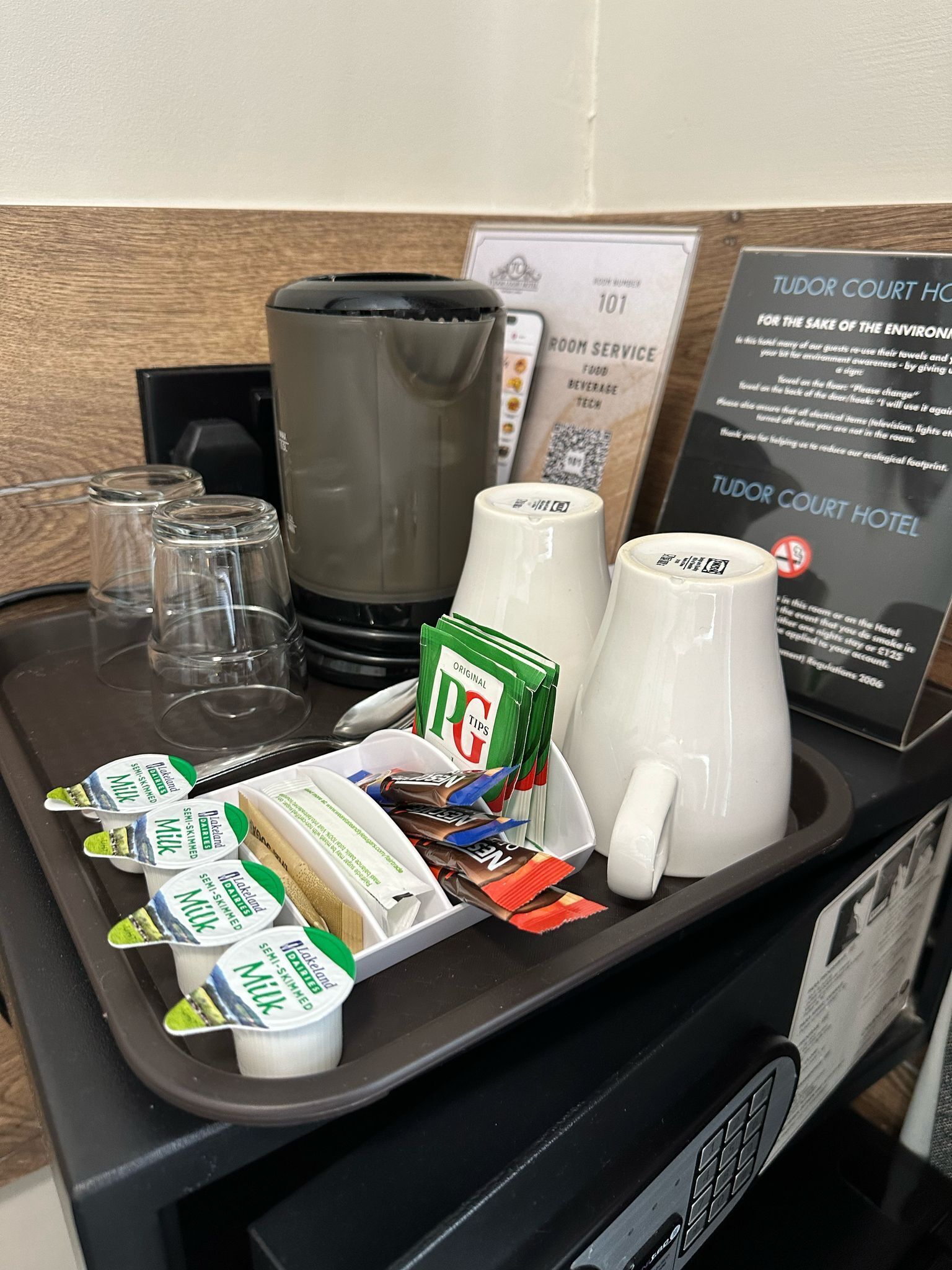 A hotel room's breakfast tray with milk packets, a coffee maker, and a sign about environmental awareness.
