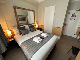 A hotel room with a large bed, a mirror, a wardrobe, and a desk with a lamp.
