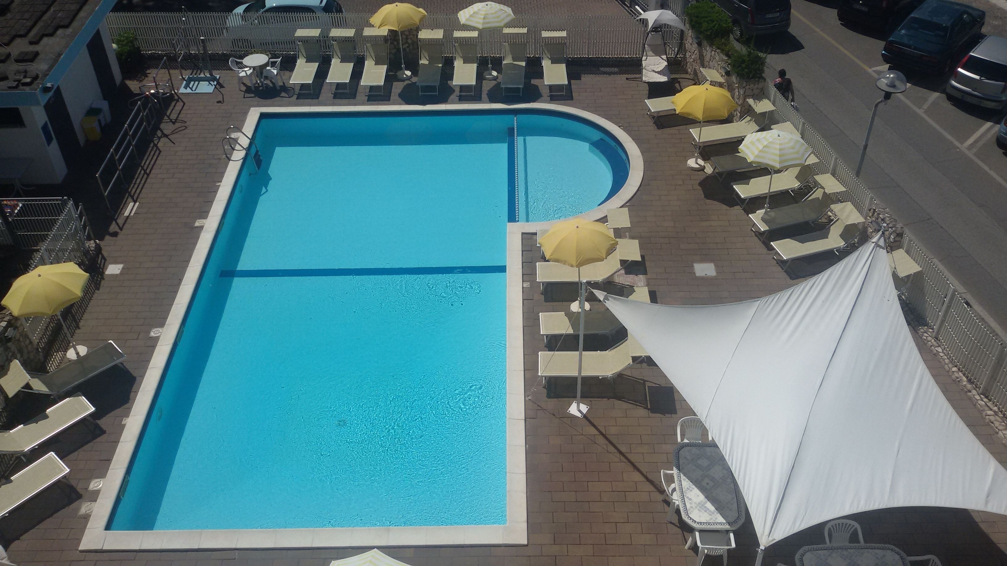 A rectangular swimming pool with a curved section, surrounded by sun loungers and umbrellas.