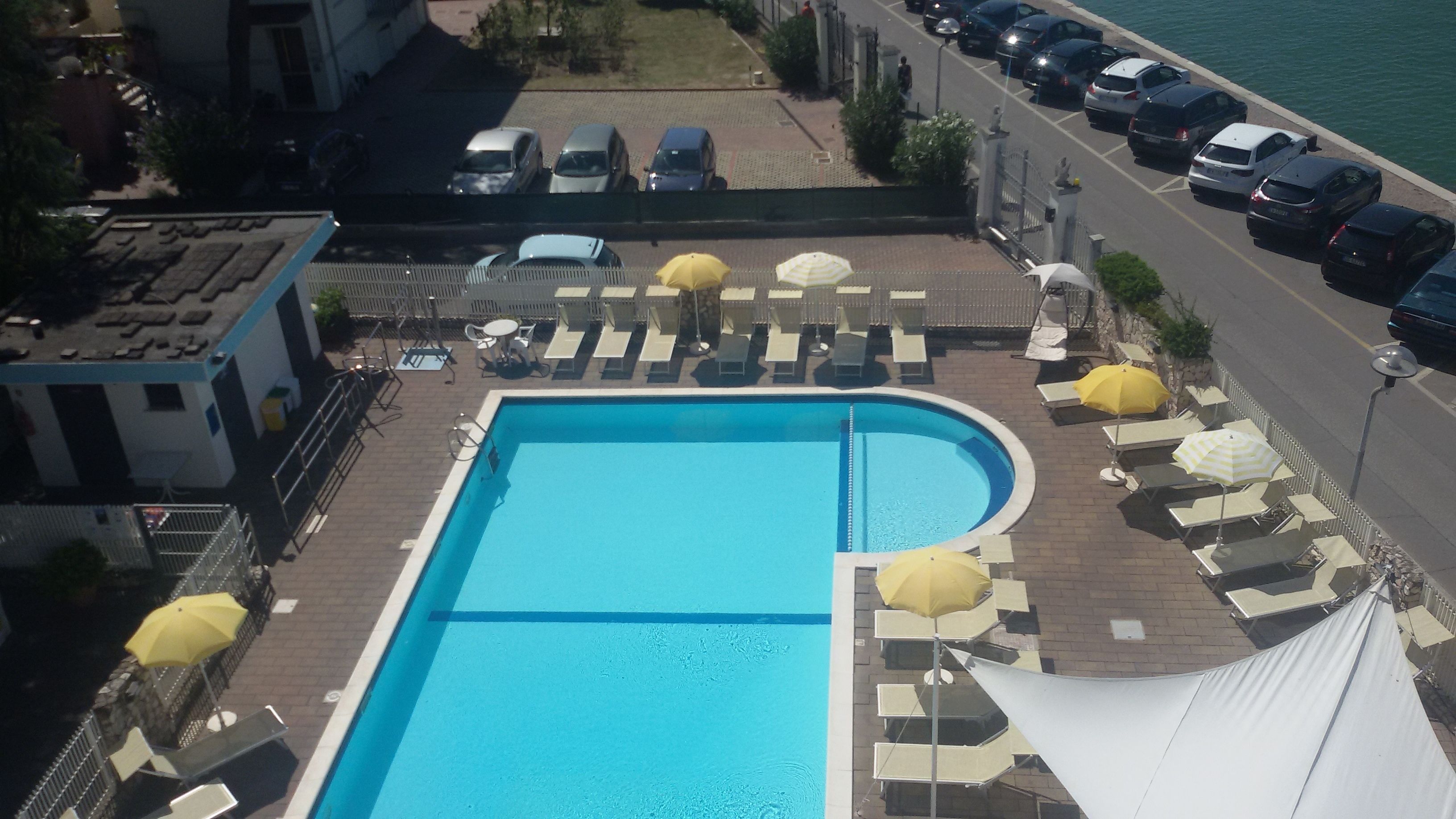 A swimming pool with sun loungers and umbrellas, surrounded by a parking area and a building.