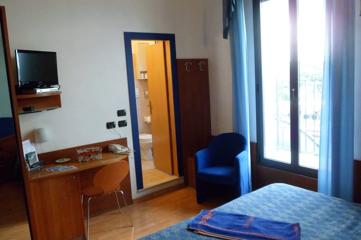 A hotel room with a bed, a desk with a chair, a television, and a wardrobe.