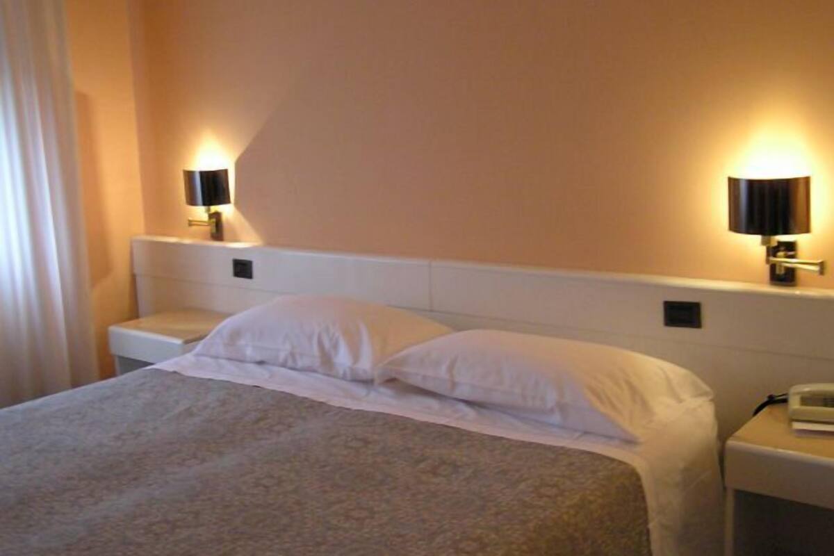 A hotel room with a bed, two bedside lamps, a nightstand, and a wall-mounted telephone.