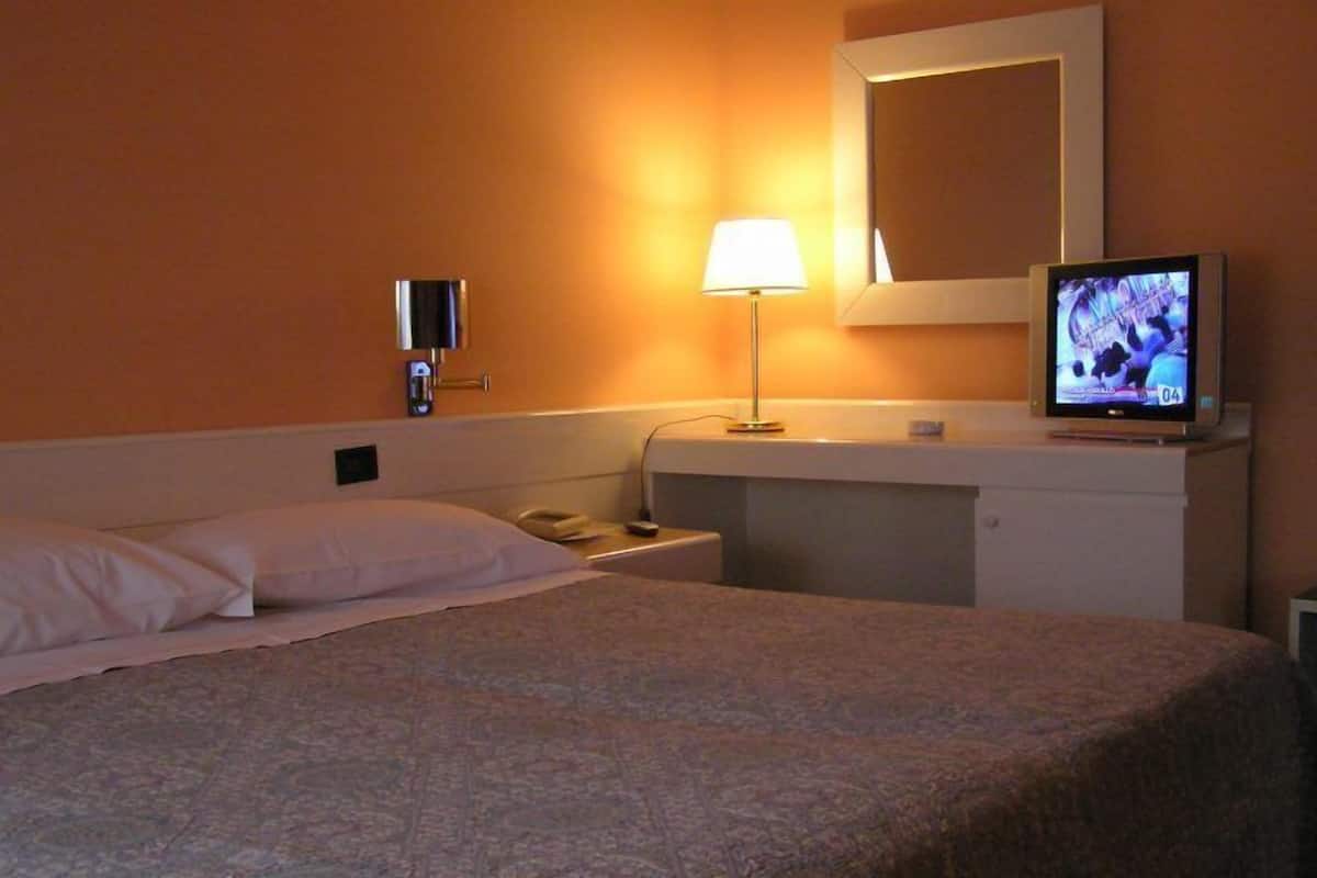 A hotel room with a bed, a nightstand, a lamp, a TV, and a mirror on the wall.
