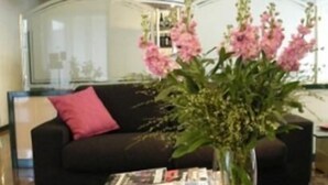 Ein Wohnzimmer mit einem schwarzen Sofa, einem Glastisch und einer Vase mit rosa Blumen.