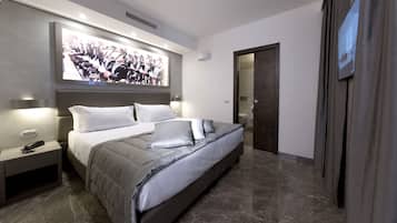 Een moderne slaapkamer met een groot bed, nachtlampen, een aan de muur bevestigde televisie en een deur naar een andere kamer.