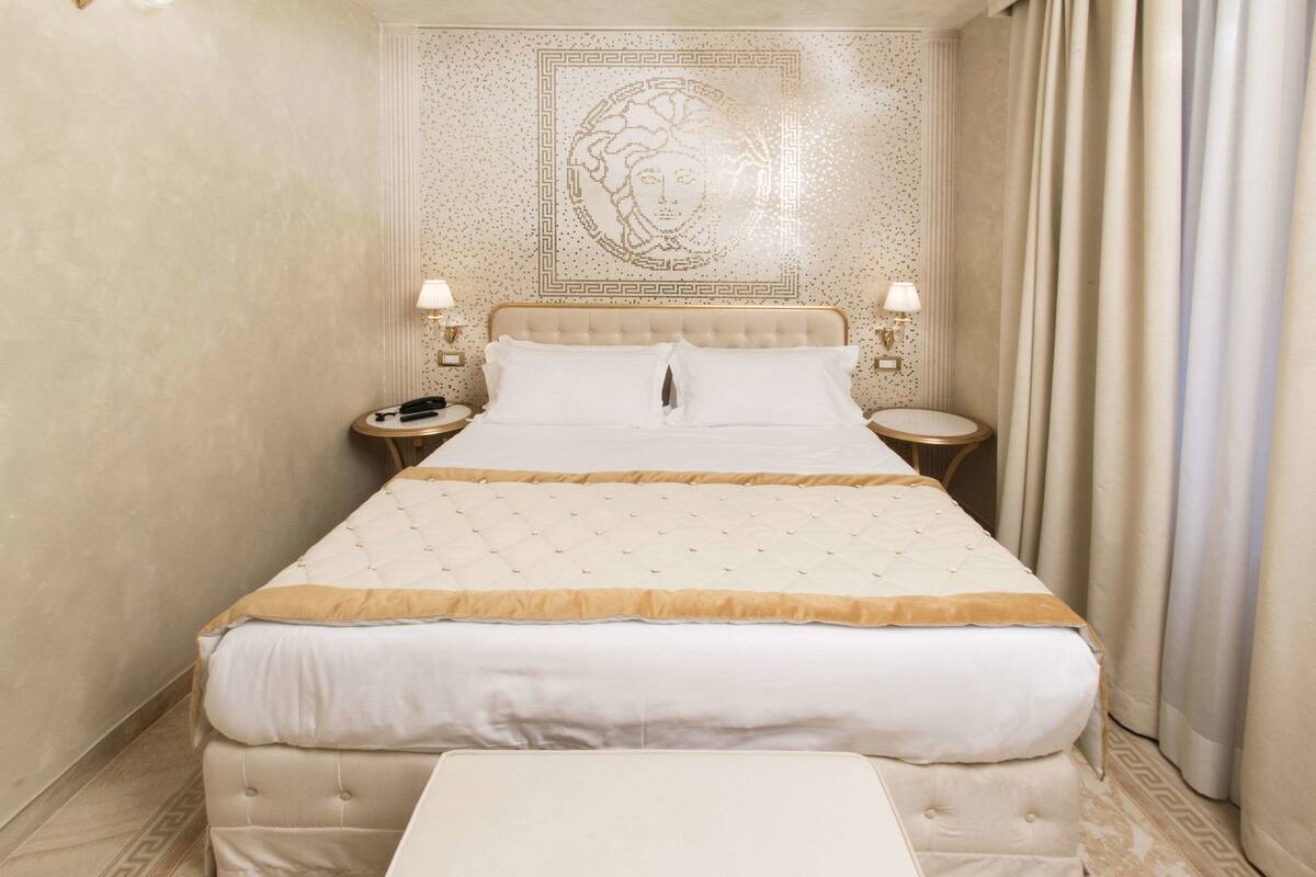 A large bed with a tufted headboard, two bedside tables with lamps, and a decorative wall panel above the bed.