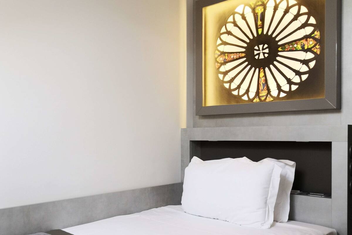 A hotel room with a bed, a headboard, and a wall-mounted decorative piece.