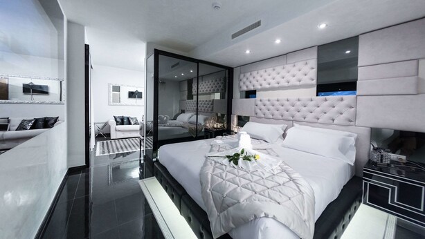A modern bedroom with a large bed, a glass partition, and a seating area with a sofa and chairs. - Best Western Premier Milano Palace Hotel (Modena)