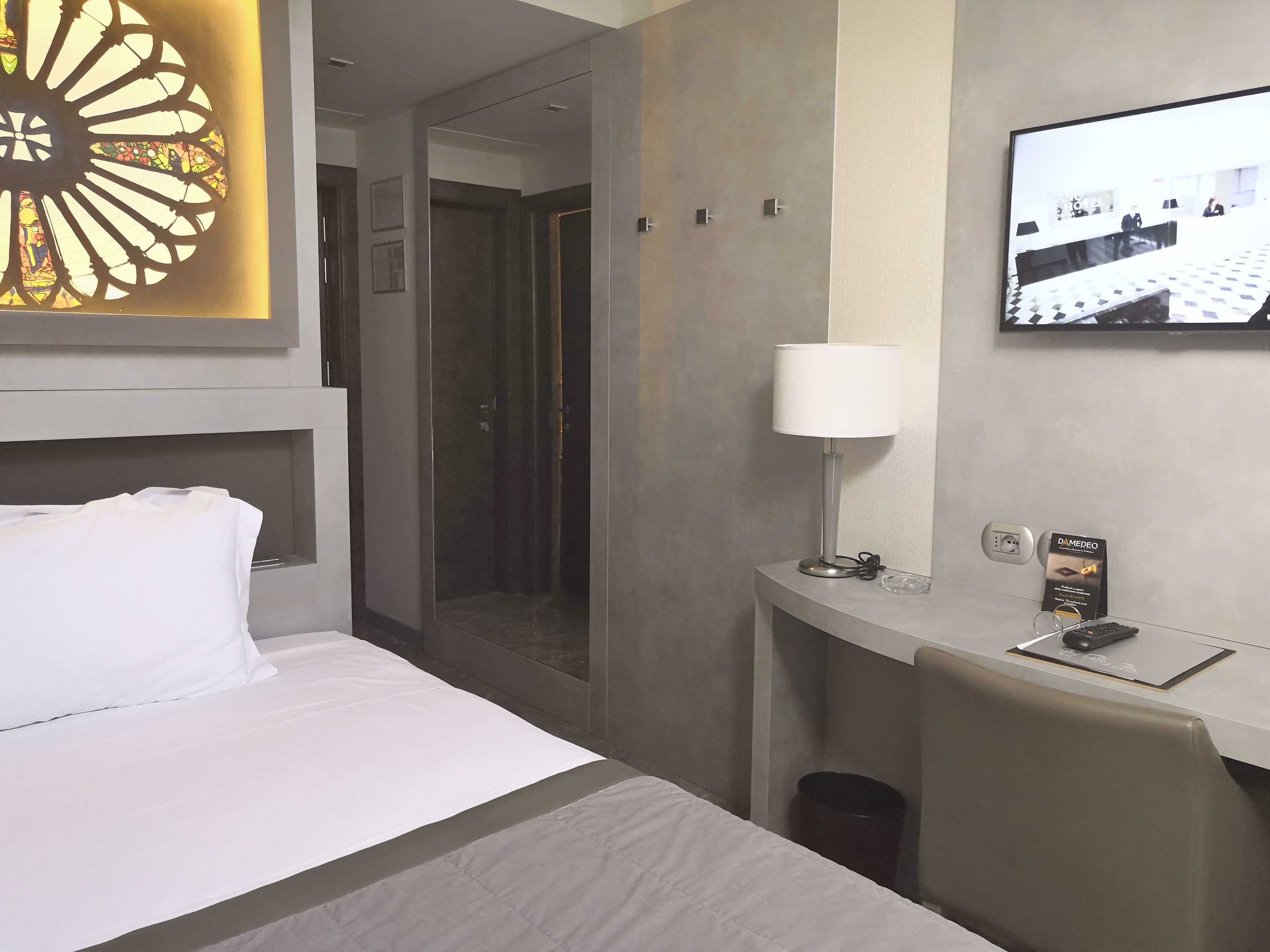 Habitació d'hotel amb un llit, una taula de nit amb làmpada, televisió i mirall.