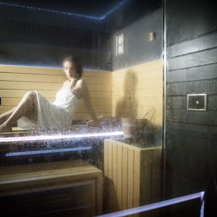 A sauna with a wooden interior, a glass door, and a control panel.