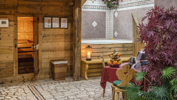 Ein Holzblockhaus-Innenraum mit Steinplattenboden, einer hölzernen Bank, einem Tisch mit Obstschale und einer Laterne.