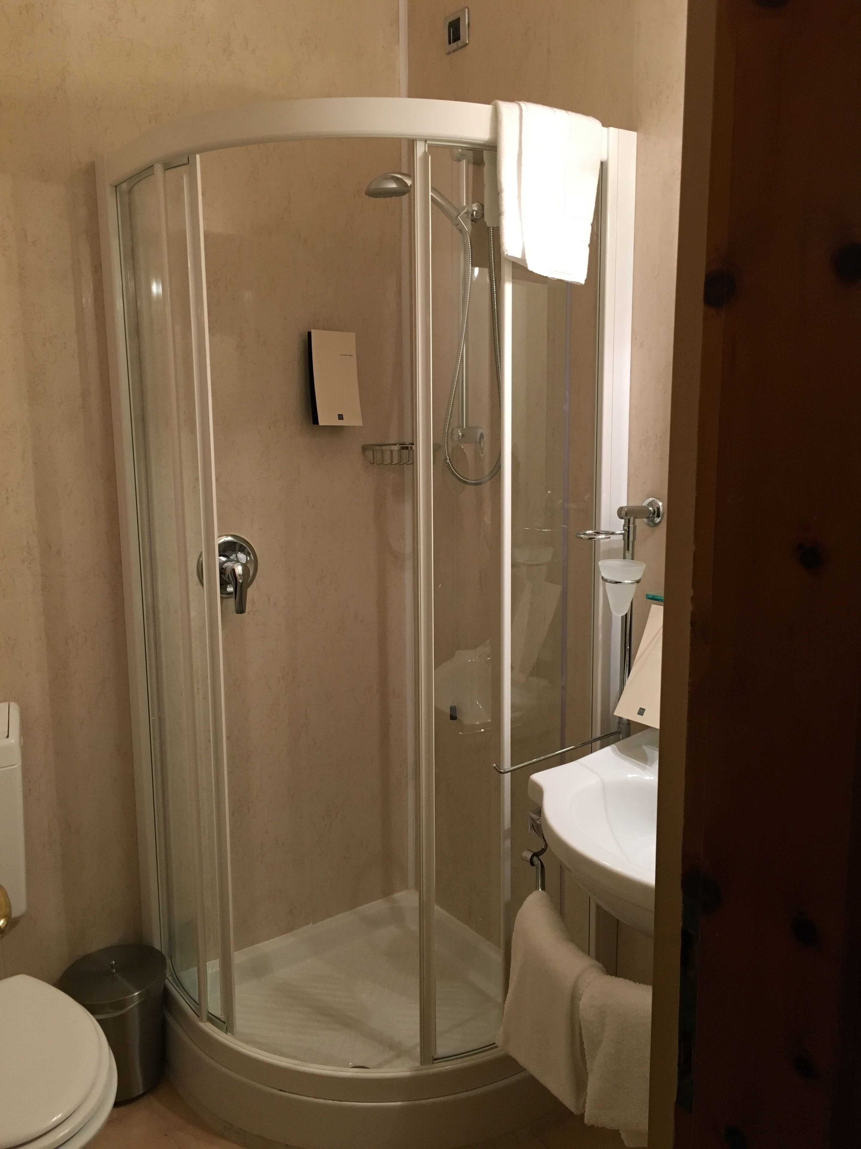 Ducha con cerramiento de vidrio, lavamanos y retrete blancos.