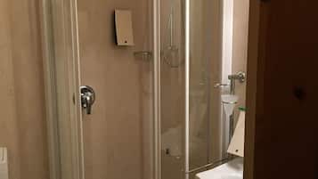 Ducha con cerramiento de vidrio, lavamanos y retrete blancos.