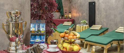 A breakfast setup with a coffee maker, cups, a fruit bowl, and a tea station.