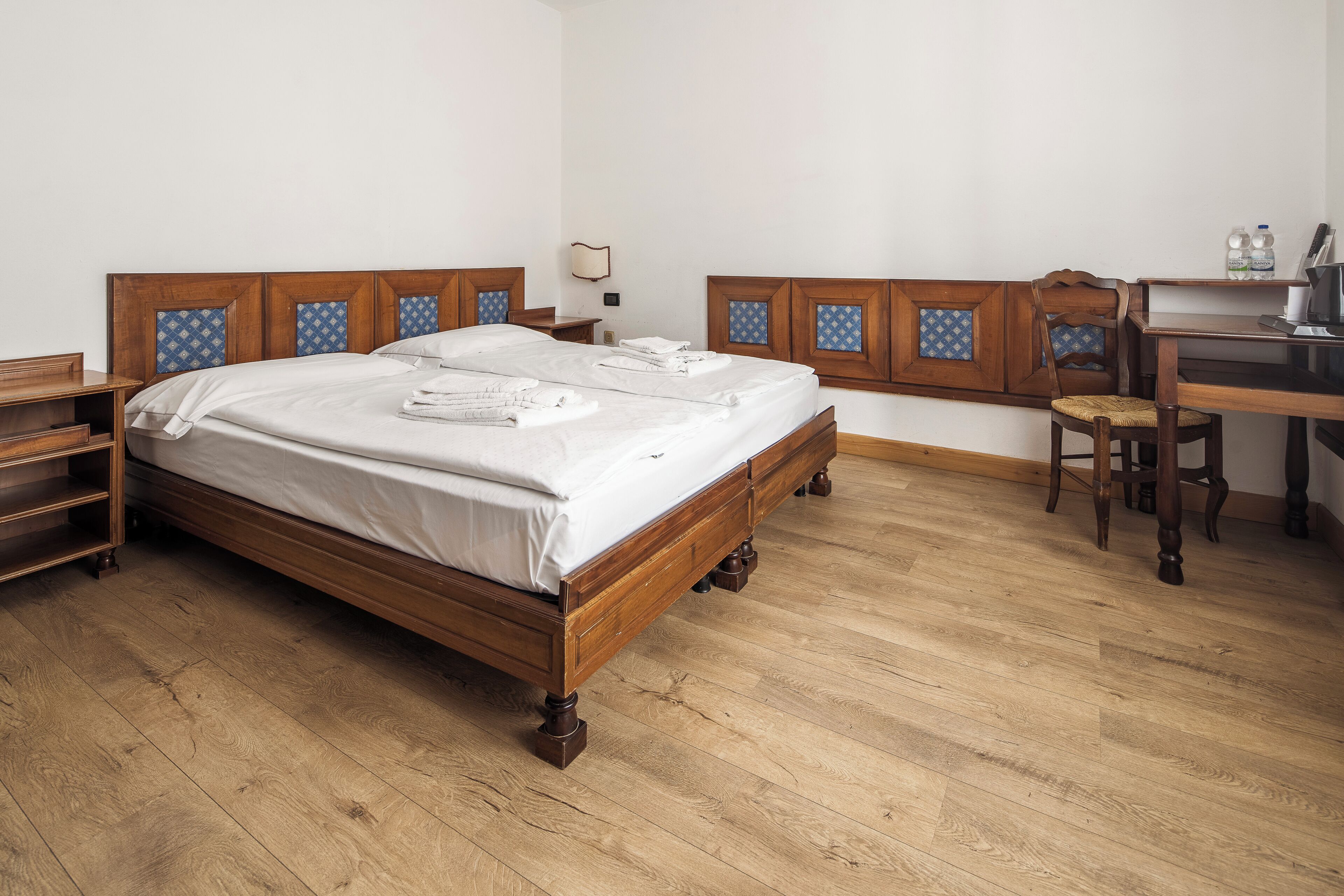 A wooden bed with a headboard, a wooden desk, a chair, and a nightstand.
