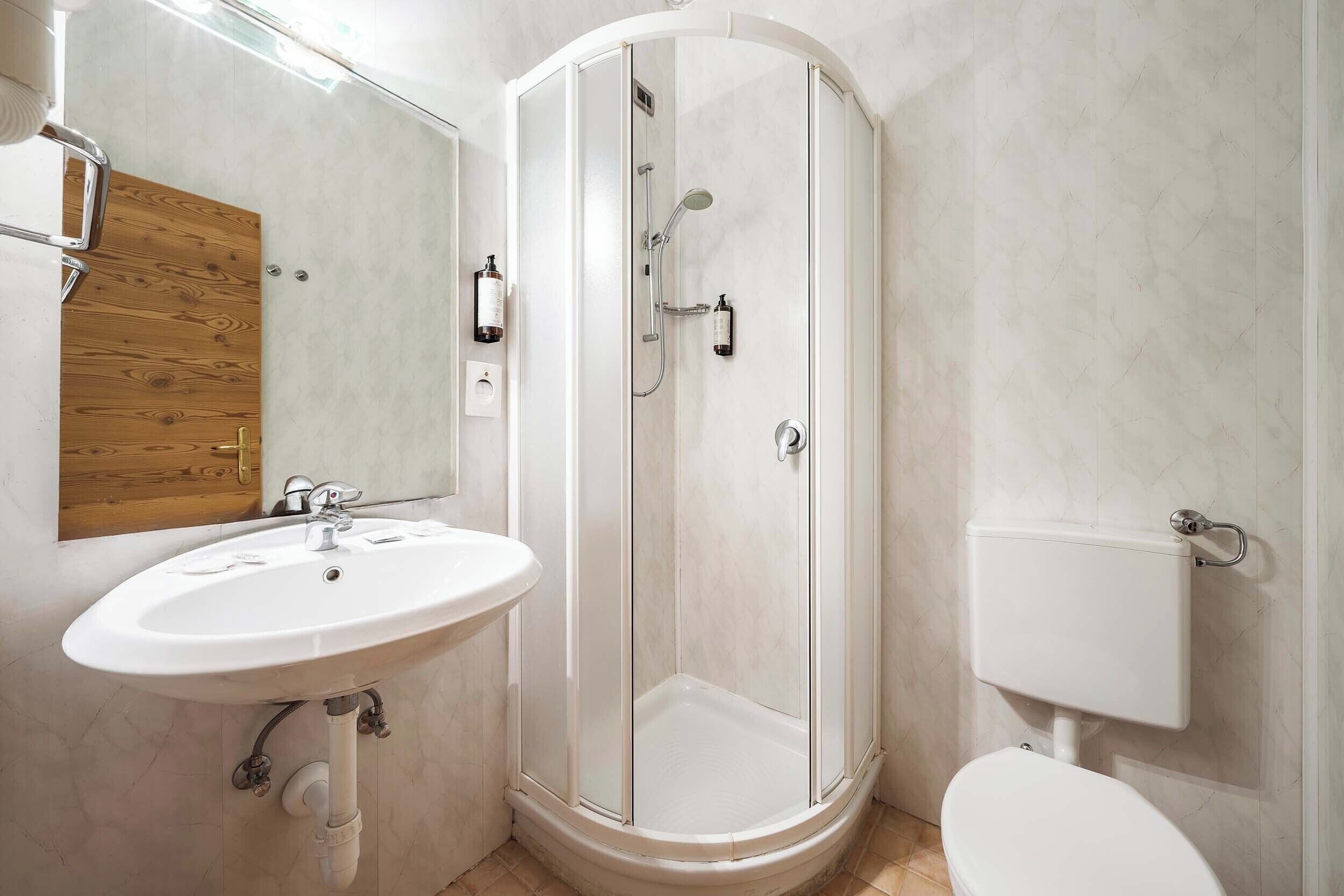 A bathroom with a white sink, a wooden door, a glass shower enclosure, and a white toilet.