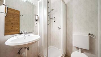 Un bagno con un lavandino bianco, una porta in legno, uno spazio doccia in vetro e un water bianco.