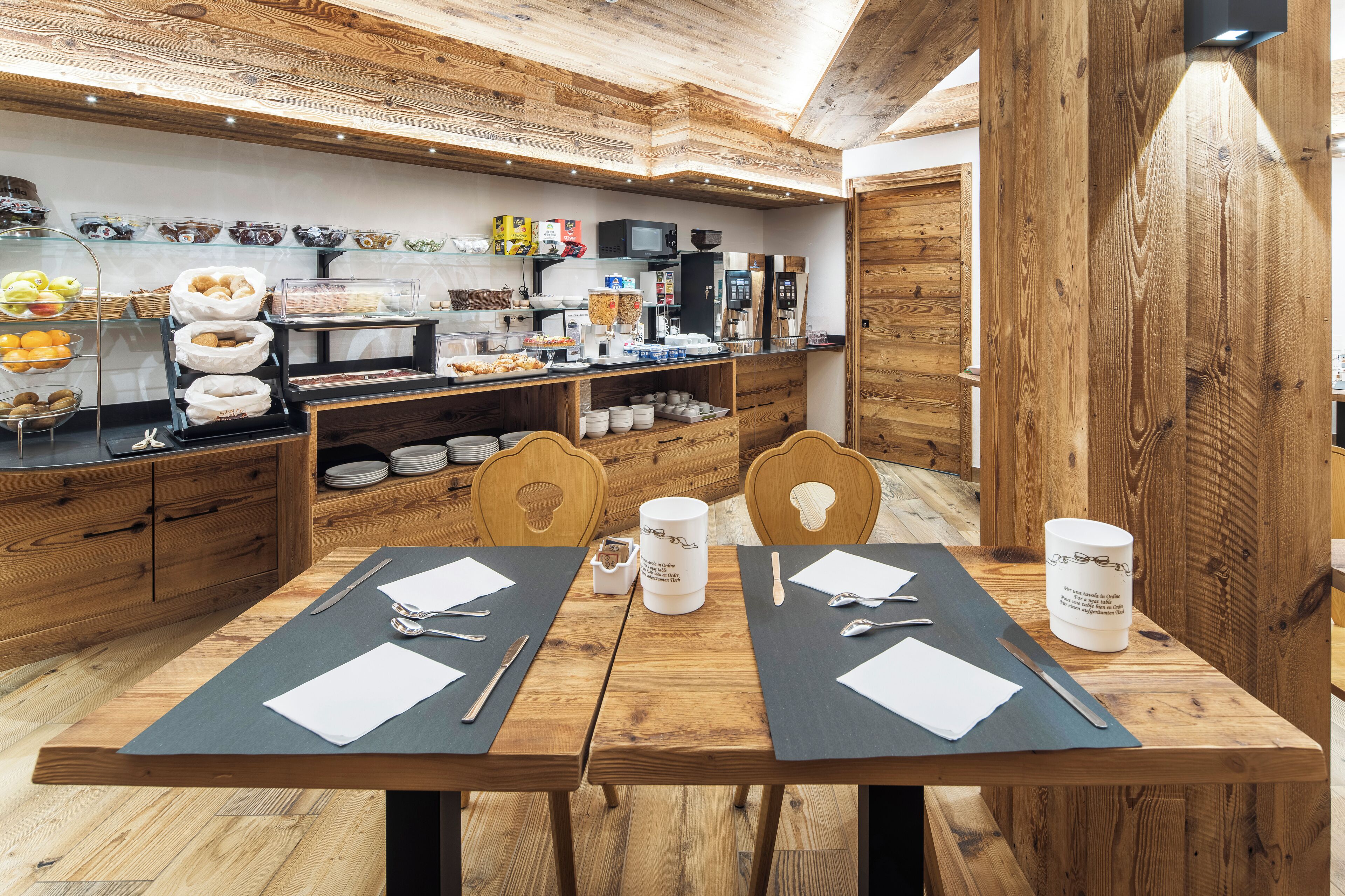 A wooden interior with a breakfast bar, wooden chairs, and a table set for two with cutlery and napkins.