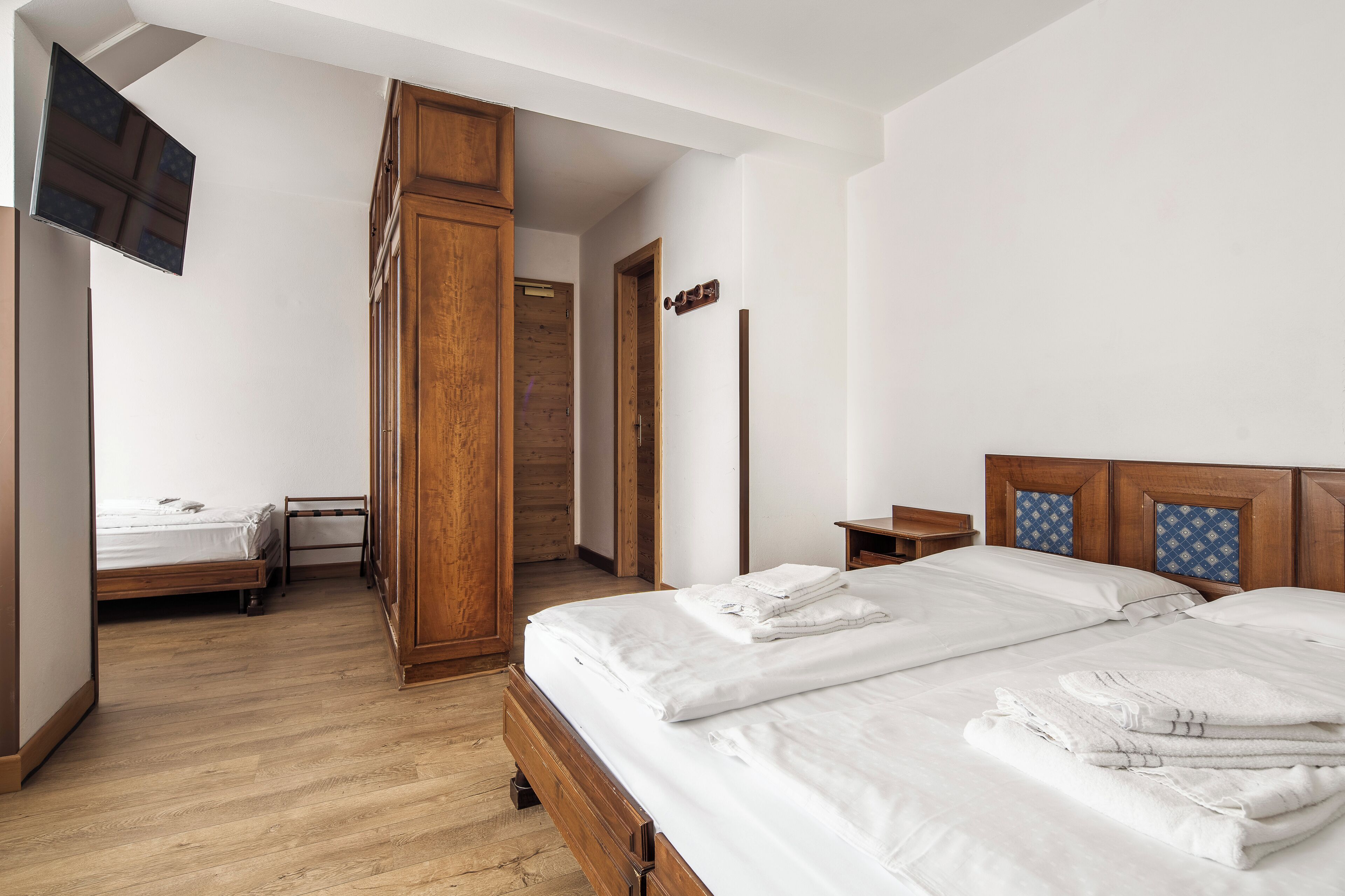 Una habitación de hotel con una cama de madera, un televisor fijado a la pared y un armario de madera.