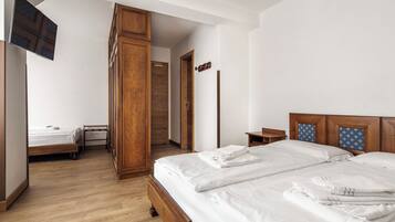 Una habitación de hotel con una cama de madera, un televisor fijado a la pared y un armario de madera.
