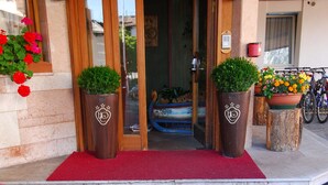 Ein Hotelzugang mit rotem Teppich, der zu einer Holztür führt, mit je einem Blumentopf auf beiden Seiten und einem Fahrrad davor.