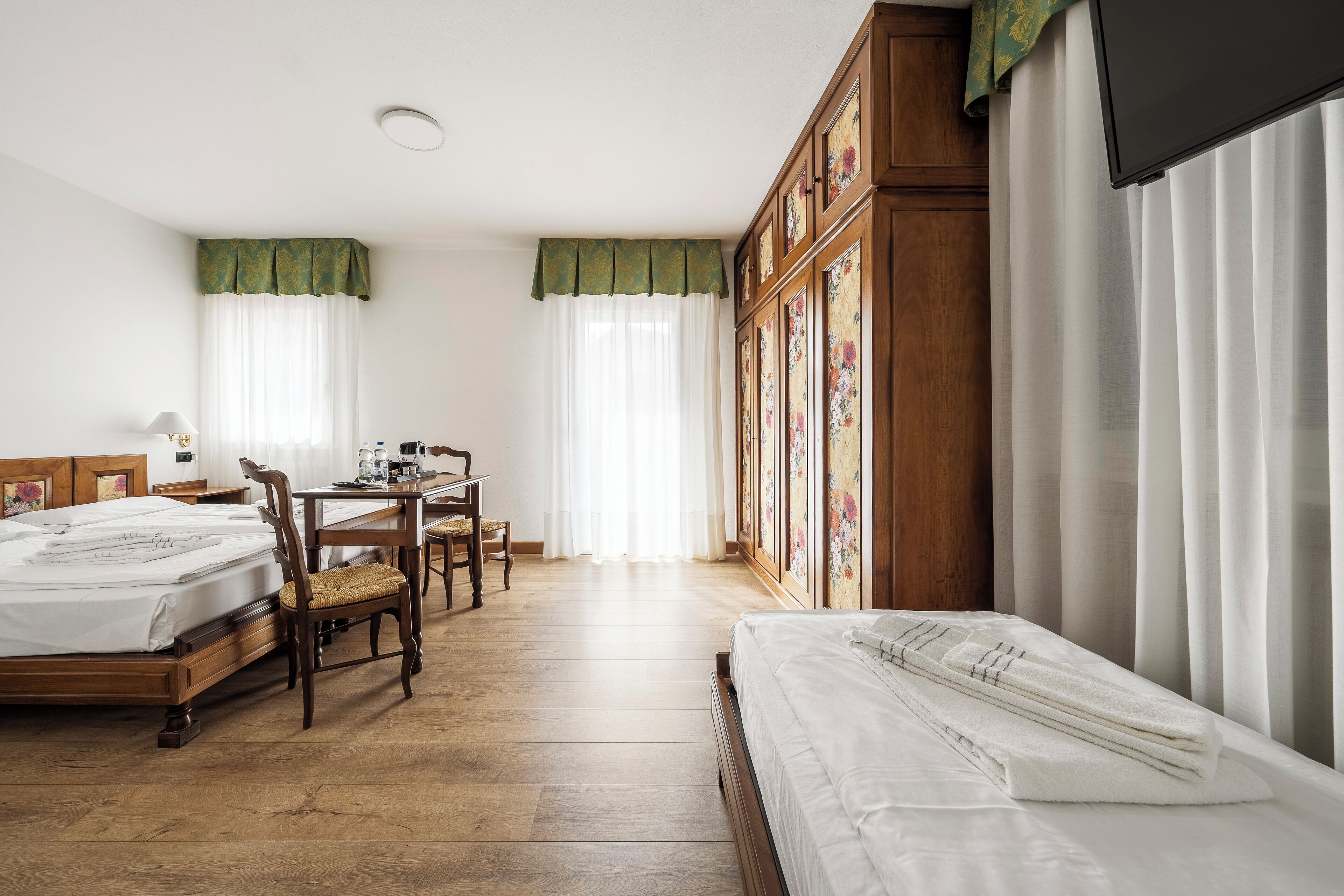 Habitación de hotel con piso de madera, dos camas, un escritorio con silla y un armario.
