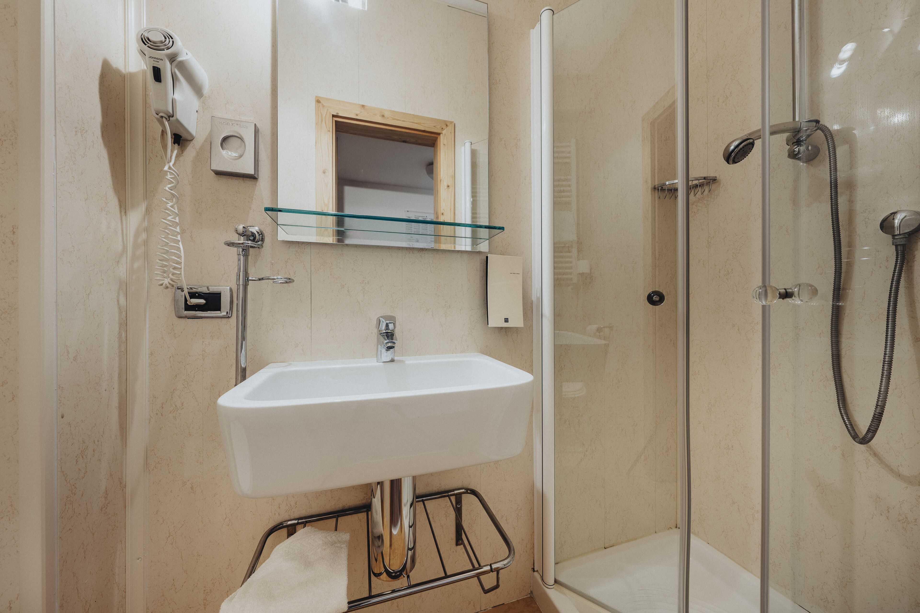 A bathroom with a glass shower enclosure, a white sink, and a hairdryer mounted on the wall.