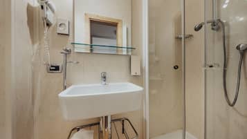 A bathroom with a glass shower enclosure, a white sink, and a hairdryer mounted on the wall.