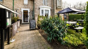 A traditional stone building with a green roof, a sign for the Leith Folk Club, and outdoor seating with umbrellas. - Victoria Park House Hotel (Edinburgh)