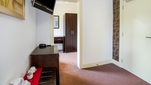 A hotel room with a flat-screen TV mounted on the wall, a wooden dresser, a red chair, a white door, and a patterned wallpaper. - Victoria Park House Hotel (Edinburgh)