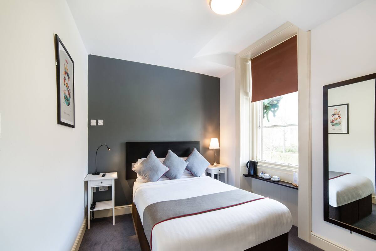A neatly arranged hotel room with a large bed, bedside tables, a nightstand, a window with a view, and a mirror.