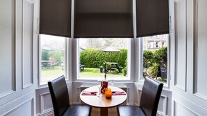 A corner room with a bay window, two black chairs, a small round table, and a view of a garden with a table and chairs outside. - Victoria Park House Hotel (Edinburgh)